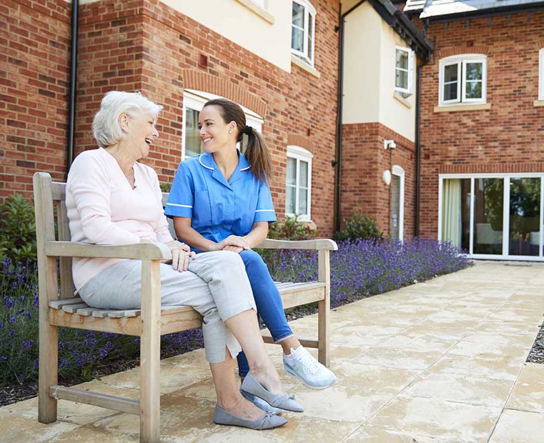 A caregiver sharing a warm, attentive moment with an older adult client at home while reviewing care notes on a tablet.
